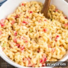 Nana's Homestyle Macaroni Salad 7 A beautifully presented bowl of creamy macaroni salad with a rustic wooden spoon, ready for serving.