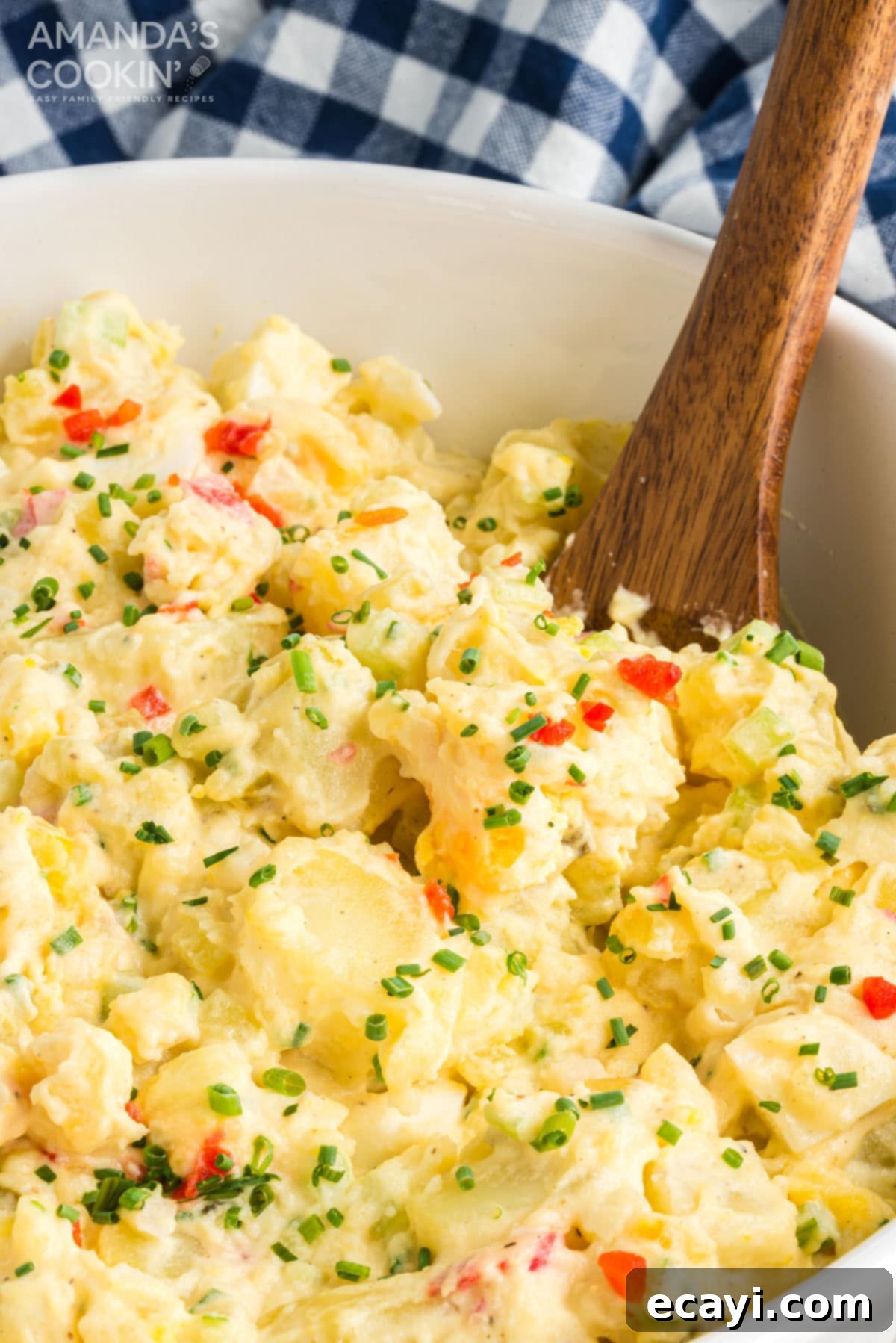 Mom's Classic Potato Salad: A creamy, flavorful, and incredibly popular recipe perfect for parties and potlucks! Wooden spoon in a large bowl of creamy potato salad, showcasing its rich texture and mixed ingredients.