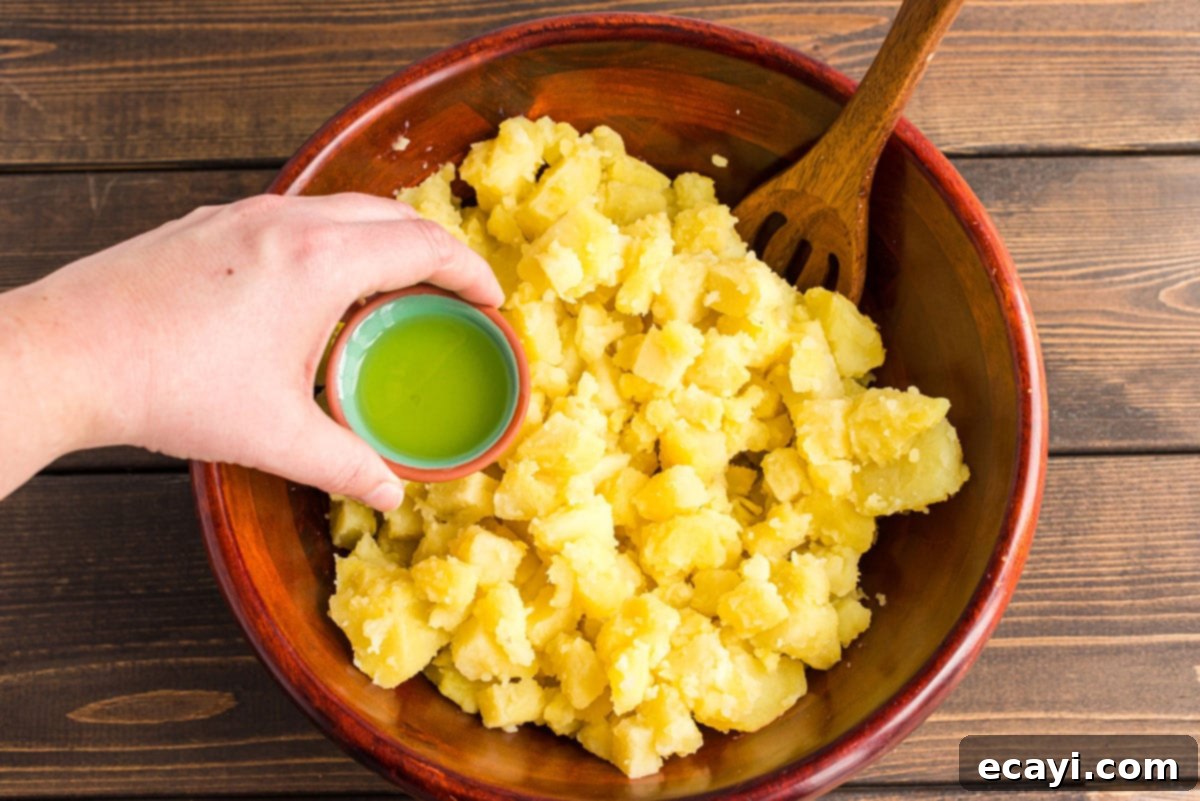 Mom's Classic Potato Salad 3 Adding pickle juice to a bowl of warm, cooked and chopped potatoes, a crucial step for flavor.