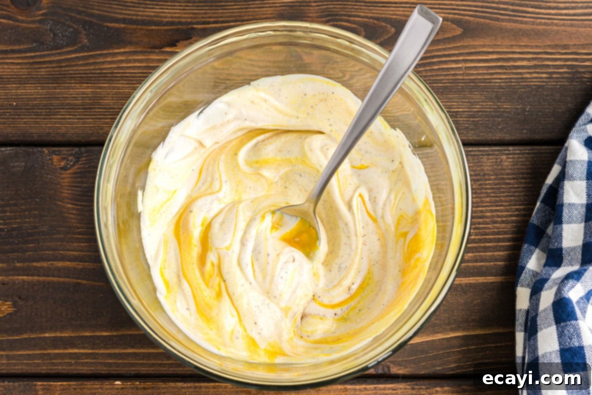Mom's Classic Potato Salad 5 A wooden spoon resting in a bowl of freshly mixed, creamy potato salad dressing.