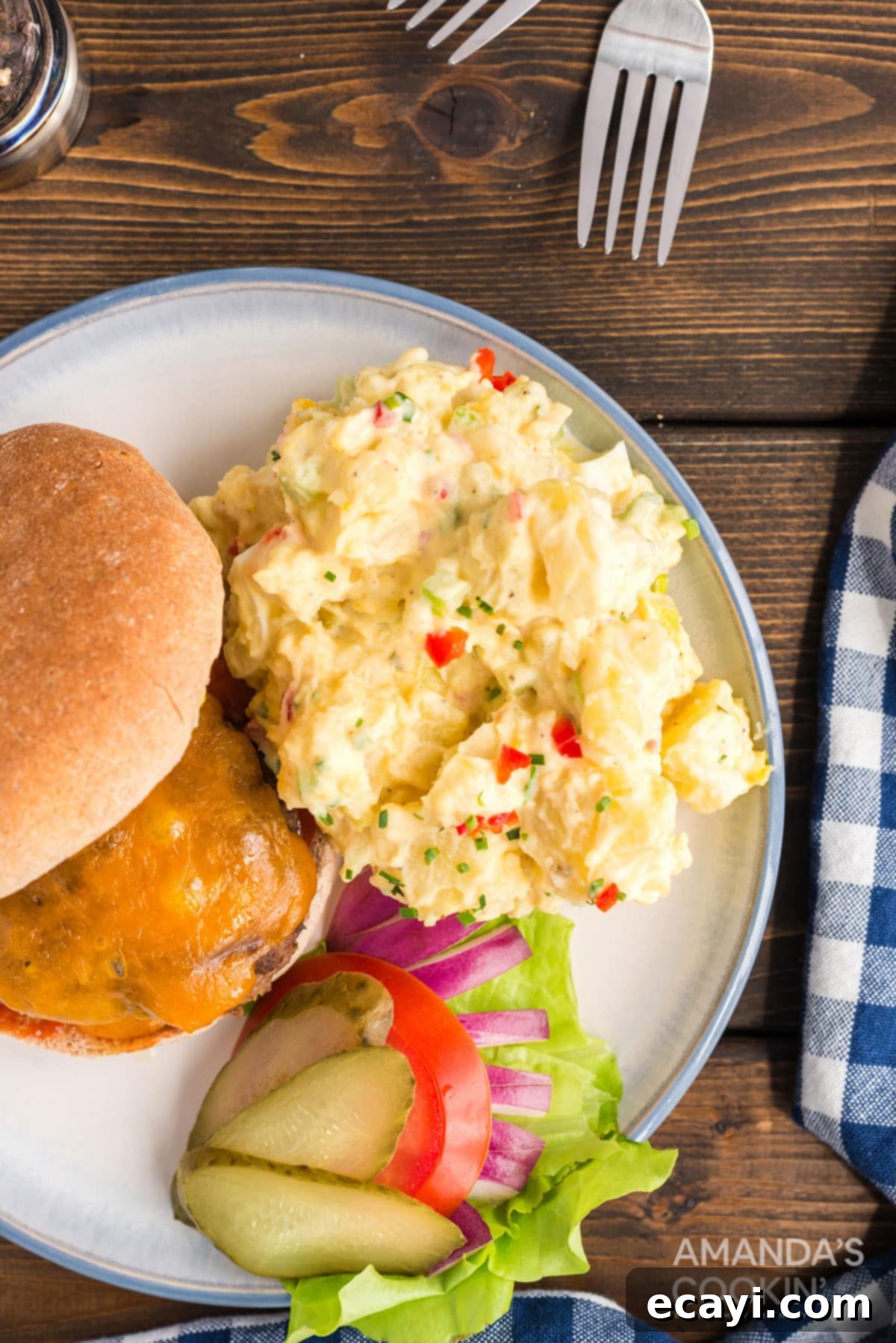 Serve this beloved potato salad alongside your favorite grilled meats for an unforgettable meal! A serving of creamy potato salad next to a grilled burger with toppings, suggesting a perfect summer meal pairing.