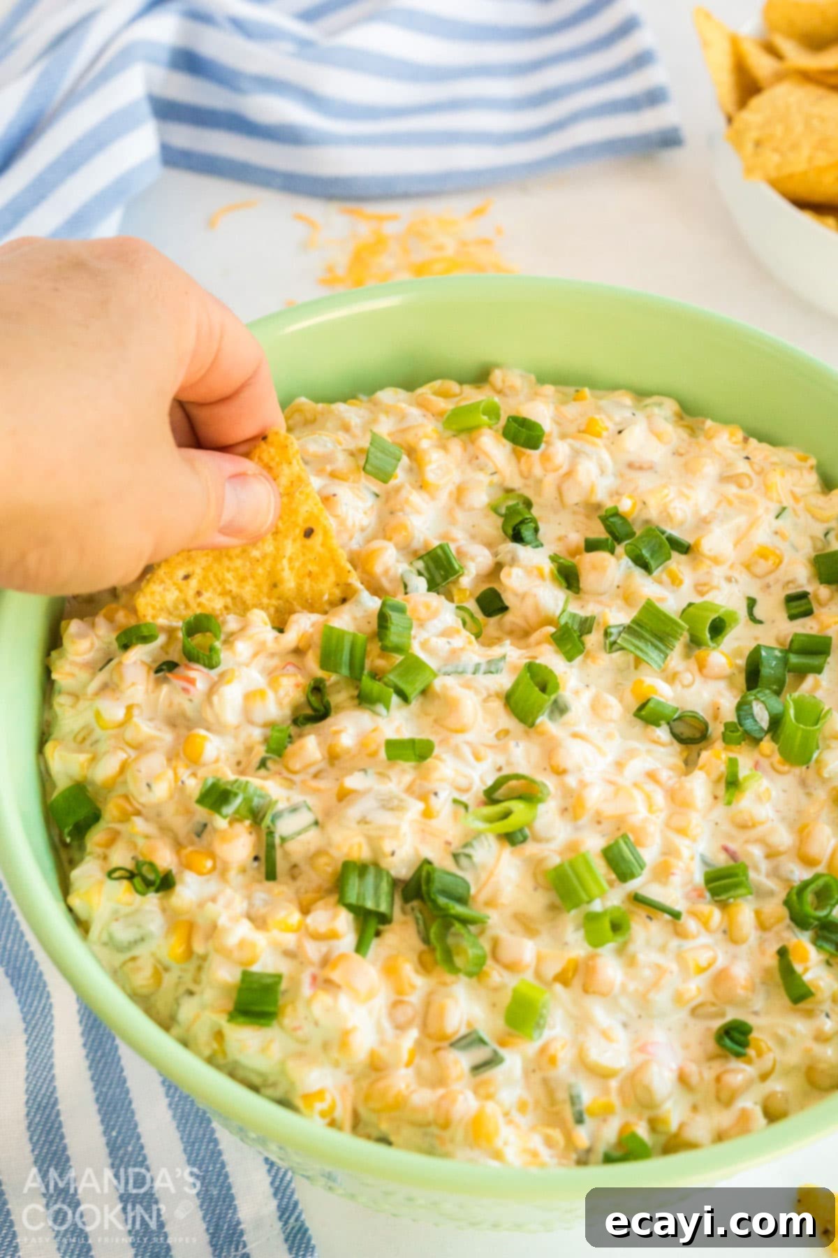 Fiesta Corn Dip 2 Hand scooping creamy corn dip with a crispy tortilla chip
