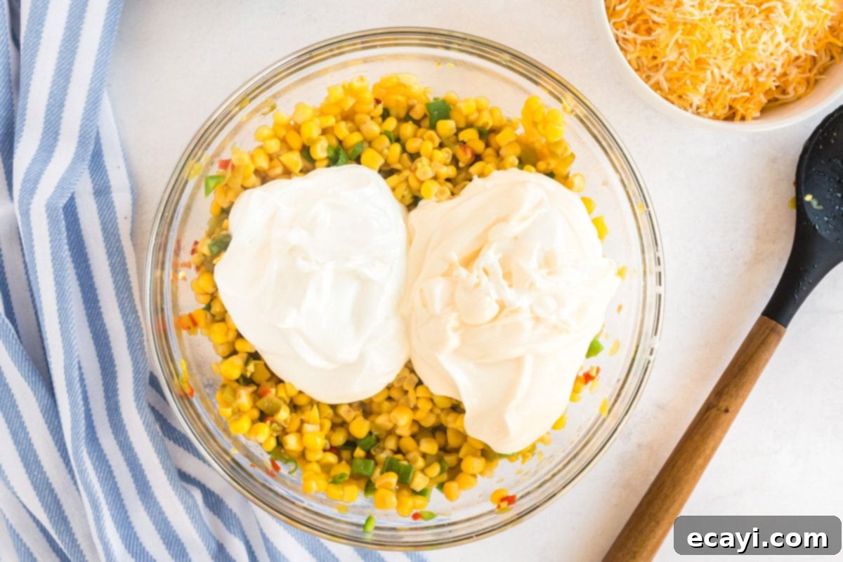 Fiesta Corn Dip 6 A bowl of corn mixture with dollops of mayonnaise and sour cream added on top, ready for stirring