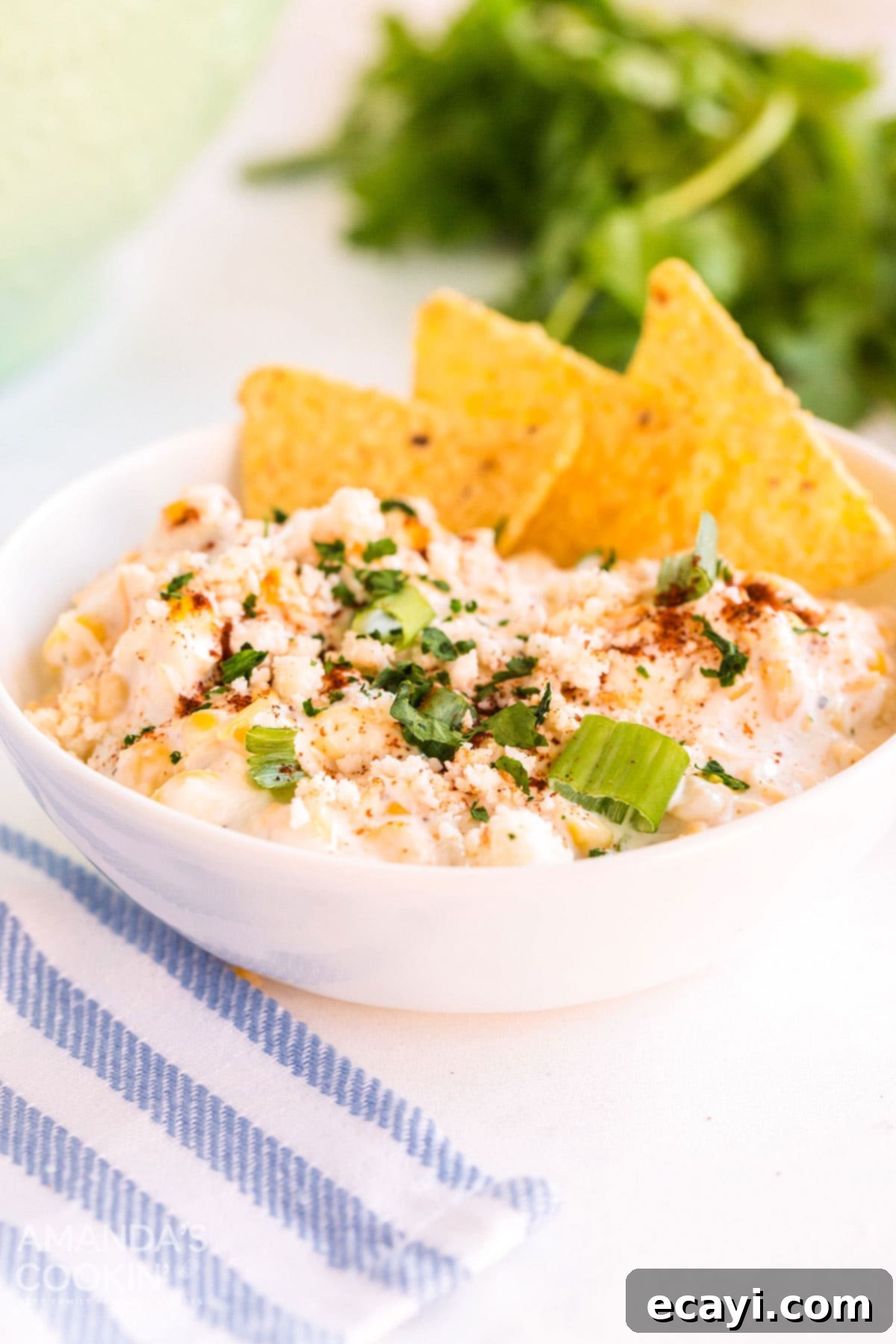 Fiesta Corn Dip 8 White bowl brimming with creamy corn dip, with several golden tortilla chips artfully placed within the dip, ready to be enjoyed