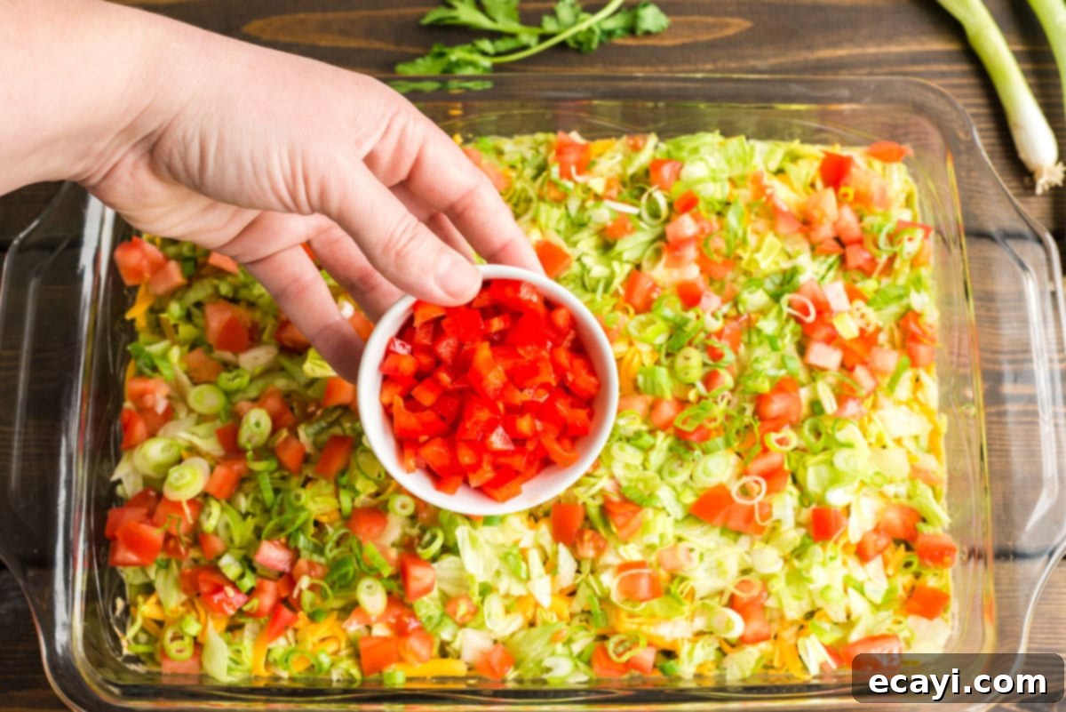 Ultimate Taco Dip 9 A vibrant, finished taco dip with all toppings sprinkled on, ready to be served with tortilla chips