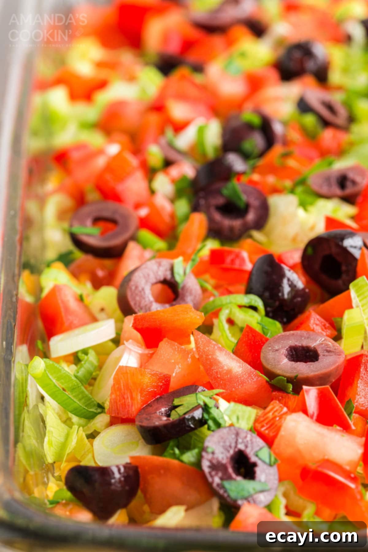 This family favorite taco dip recipe uses refried beans, guacamole, sour cream, cream cheese, taco seasoning and plenty of crunchy toppings. The perfect party dip! Close-up view of a perfectly layered taco dip, showing off the vibrant colors and fresh textures of all seven layers.