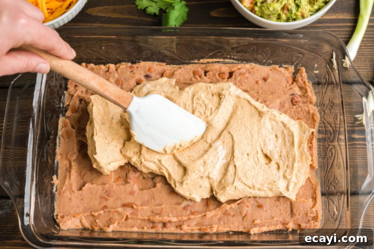 Ultimate Taco Dip 6 Carefully spreading the creamy, seasoned cream cheese and sour cream mixture over the refried bean base in a glass pan