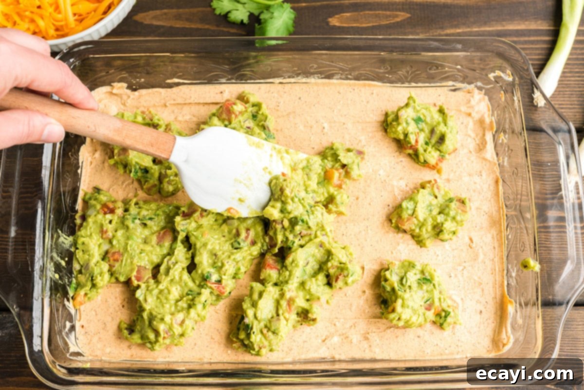 Ultimate Taco Dip 7 Spreading fresh guacamole over the seasoned sour cream and cream cheese layer in the baking pan for the taco dip