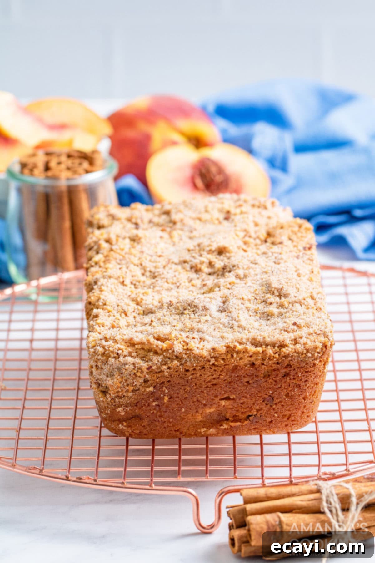 The delicious peach bread is studded with almonds and topped with an amazing cinnamon almond mixture you will love. A freshly baked loaf of cinnamon almond peach quick bread, golden brown and perfectly risen, resting on a wire cooling rack on a wooden surface.