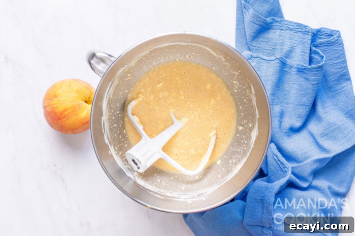 Golden Peach Loaf 3 Close-up shot of creamy, pale yellow batter being mixed in a clear glass bowl with a paddle attachment of a stand mixer, demonstrating the initial wet ingredients blending phase.