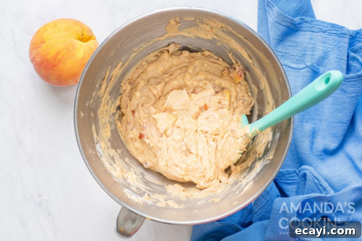Golden Peach Loaf 5 Close-up of peach bread batter in a mixing bowl after all ingredients have been combined, showing the chunks of peaches and almonds evenly distributed within the thick, creamy batter.