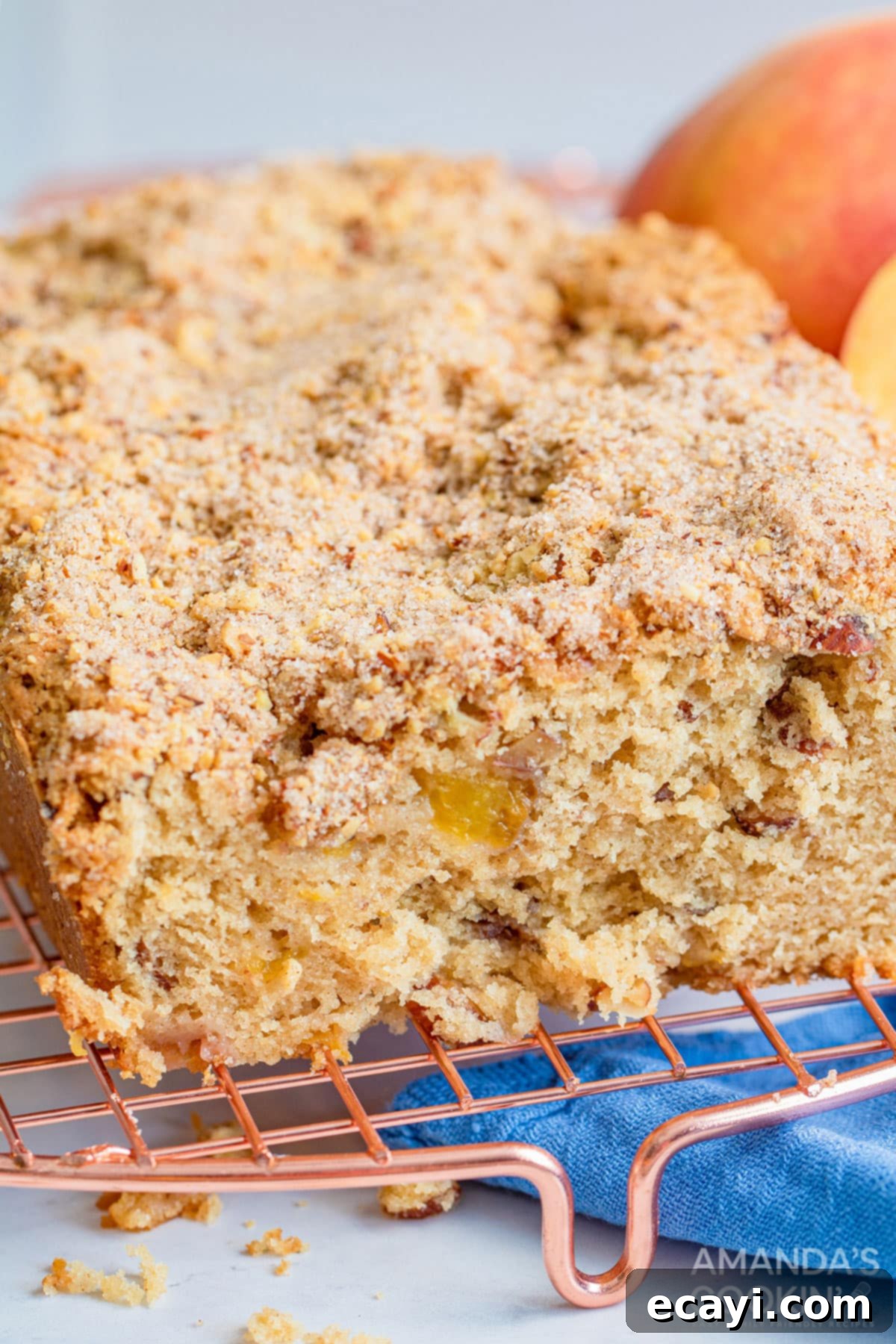 The delicious peach bread is studded with almonds and topped with an amazing cinnamon almond mixture you will love. A close-up view of a perfectly sliced peach quick bread, revealing the moist crumb, chunks of sweet peaches, and the embedded almonds, ready to be enjoyed.