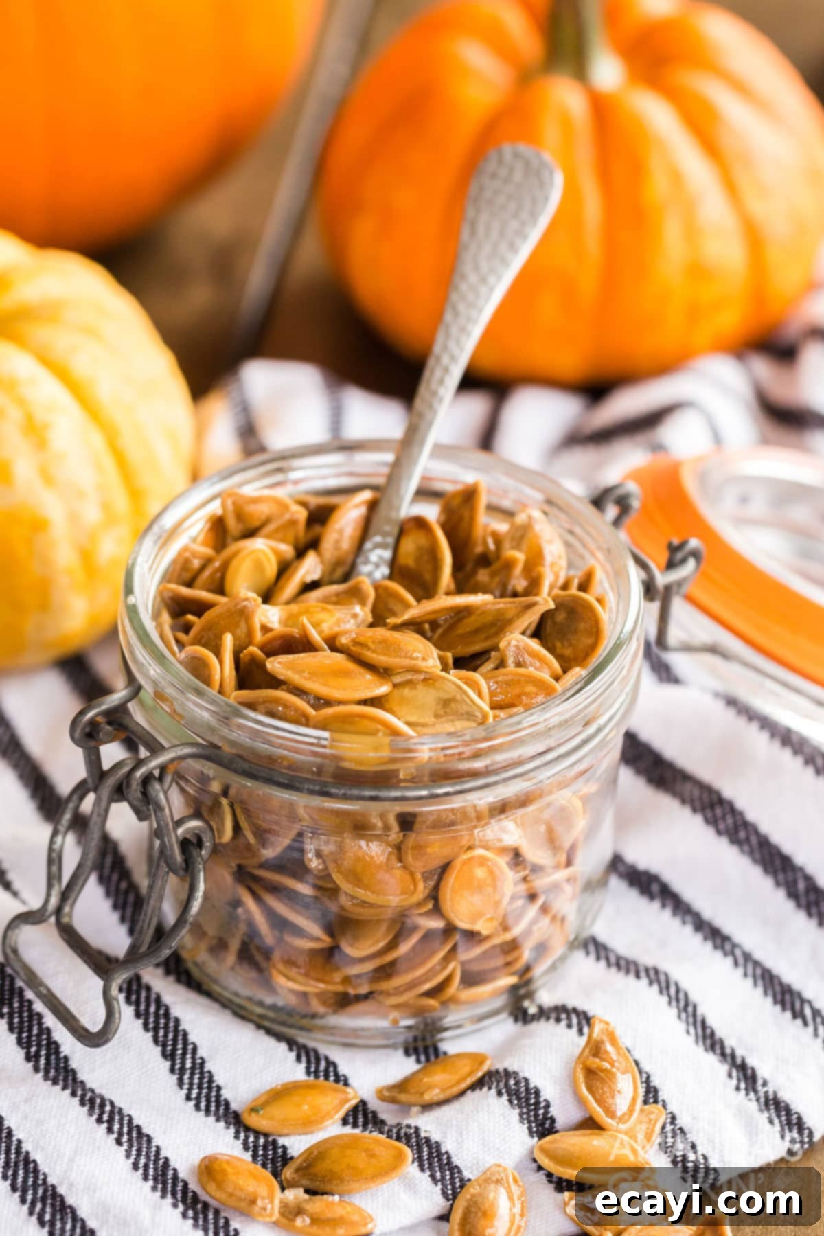 Perfectly Roasted Pumpkin Seeds: Your Go-To Fall and Halloween Snack A small glass jar filled with perfectly roasted pumpkin seeds, with a wooden spoon resting inside, ready for snacking.