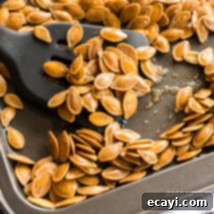 Crispy Roasted Pepita Snack 3 A baking sheet with freshly roasted pumpkin seeds and a serving spatula.