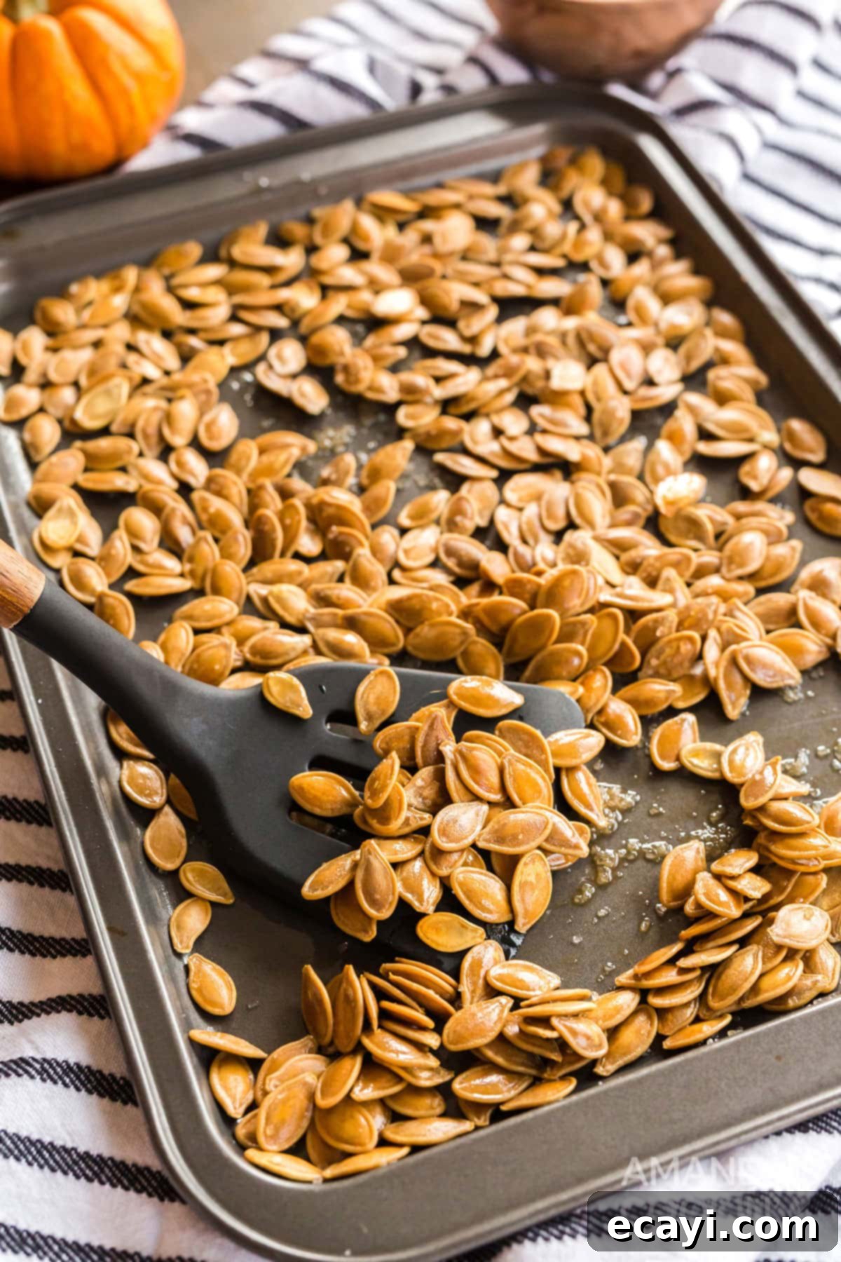 Easy Roasted Pumpkin Seeds: A Healthy and Delicious Fall Treat A baking sheet overflowing with freshly roasted, golden-brown pumpkin seeds, alongside a spatula ready to serve them.