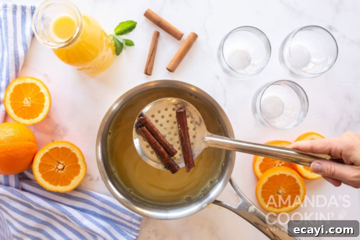 Velvet Orange Vanilla Punch 3 Straining cinnamon sticks from the simmering orange juice mixture in a saucepan after infusion