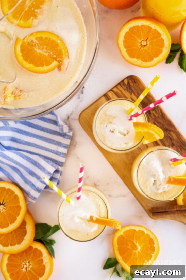 With only four ingredients you can make this creamy, dreamy, vanilla orange punch. Whether it's in the fall, summer, or spring, it's delicious year-round! Large punch bowl filled with frothy vanilla orange punch, with individual serving glasses and garnishes next to it