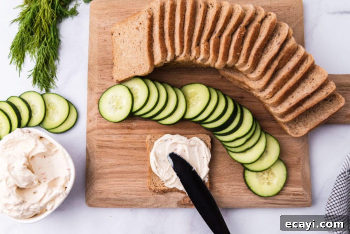 Delicate Cucumber Finger Sandwiches 5 A hand spreading cream cheese evenly on a slice of cocktail rye bread, a crucial step in preparing mini cucumber sandwiches.