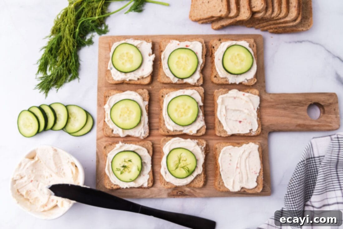 Delicate Cucumber Finger Sandwiches 6 An overhead view capturing the process of assembling mini cucumber sandwiches, showing cucumber slices being placed on cream-cheese-spread bread.