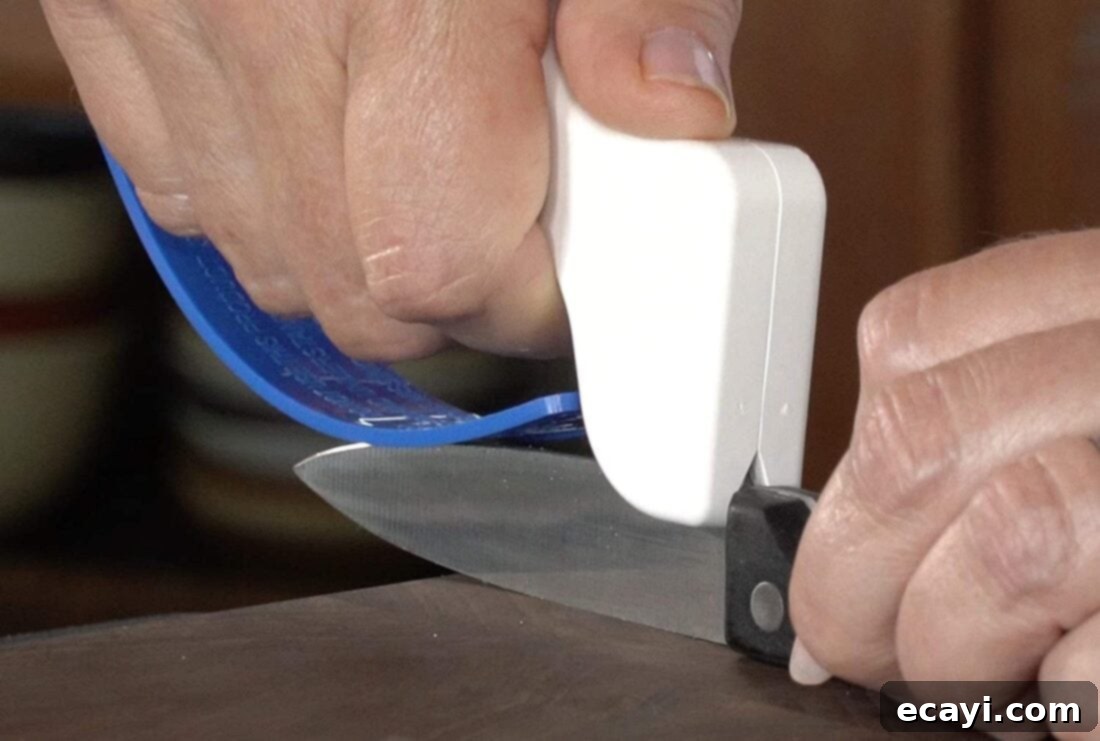 21 Kitchen Gadgets You'll Reach For Daily 3 A hand demonstrating the use of a knife sharpener, carefully sharpening a chef's knife blade with precision and safety.