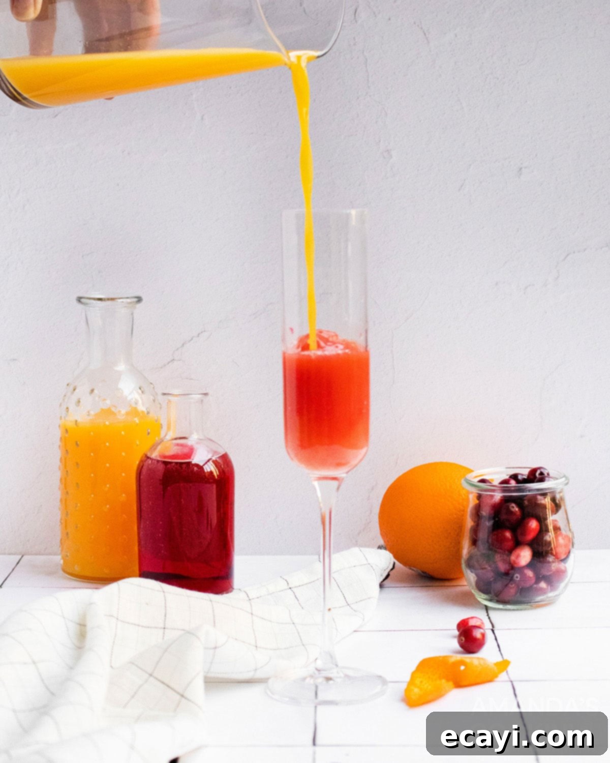 Sparkling Cranberry Mimosa 4 Pouring fresh orange juice into a champagne flute with cranberry juice