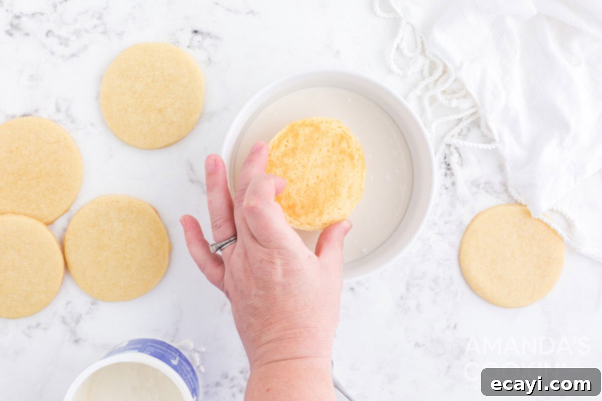 Sweet & Simple Decorated Cookies 12 A round sugar cookie being carefully dipped face-down into a bowl of melted white frosting.