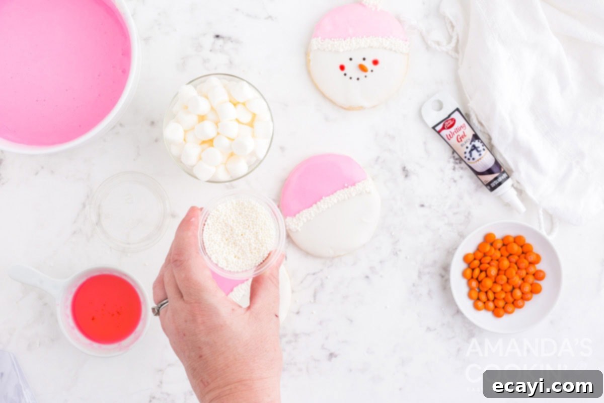 Sweet & Simple Decorated Cookies 15 A hand sprinkling white nonpareils onto the piped frosting on a snowman cookie.