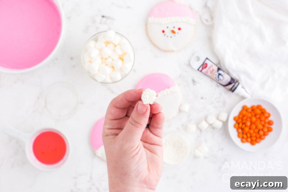 Sweet & Simple Decorated Cookies 16 A hand holding a mini marshmallow, which has one end covered in white frosting and nonpareils, ready to be placed on a cookie.