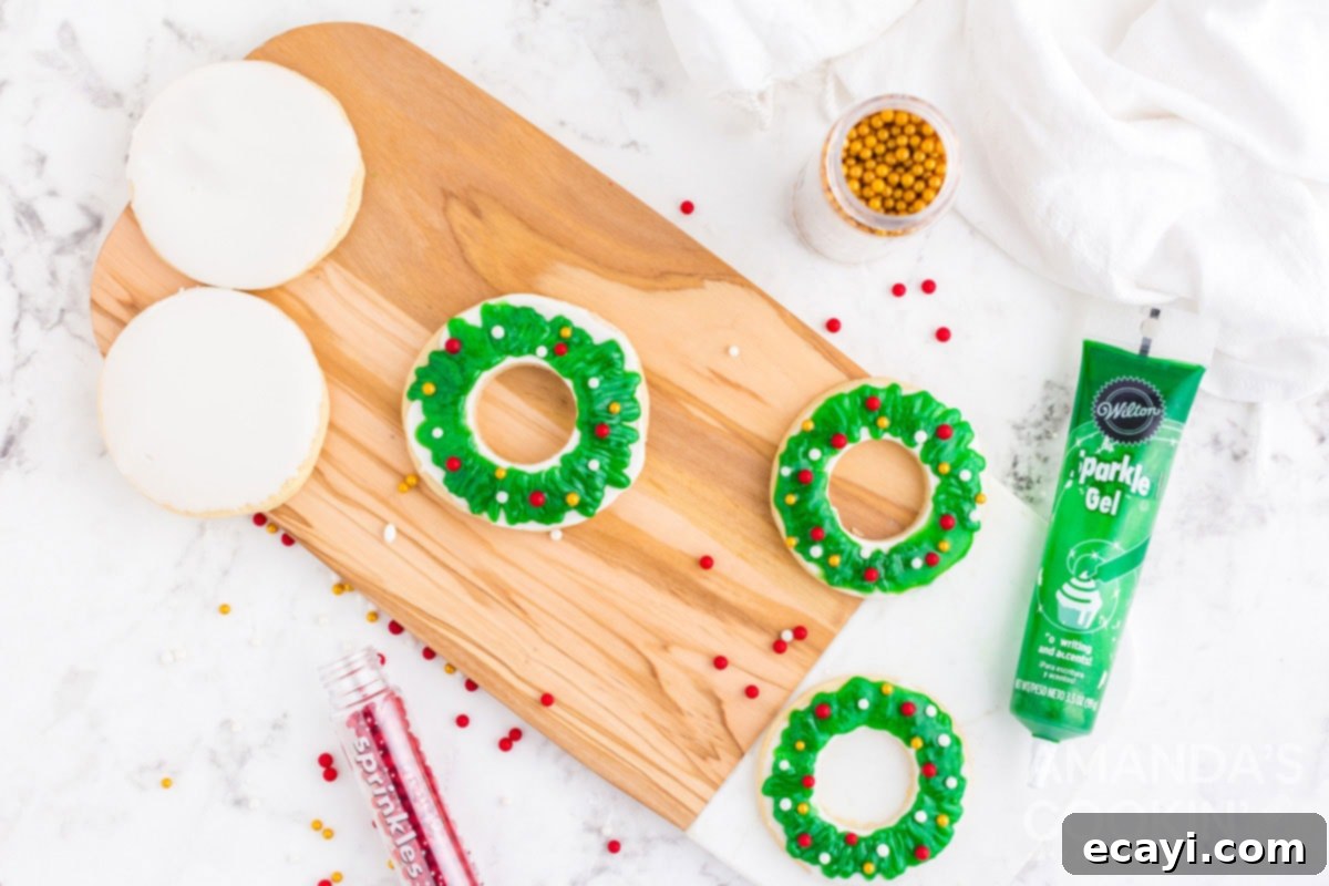 Sweet & Simple Decorated Cookies 21 A hand applying green sparkle gel in a zig-zag pattern onto a white-iced, wreath-shaped sugar cookie.
