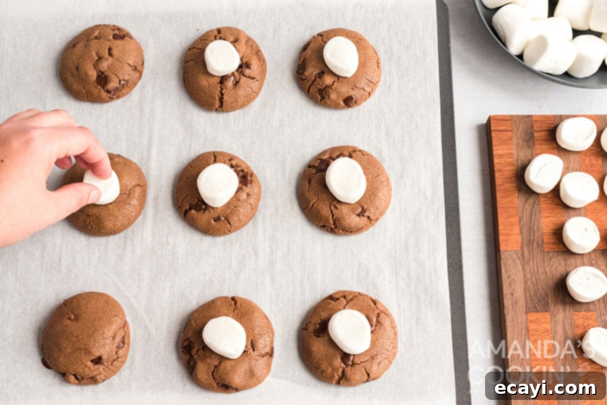 Cozy Cocoa Cookies 13 Gently pressing halved marshmallows onto hot, freshly baked cookies for their final bake.