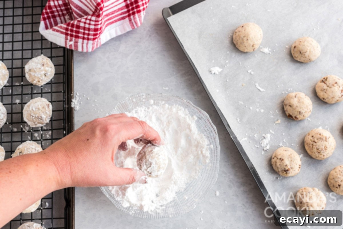 Snowball Cookies 12 Rolling warm snowball cookies in a bowl filled with powdered sugar, ensuring a thorough and even coating