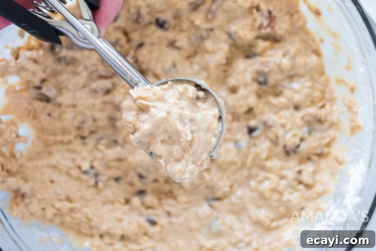 Chewy Oat Delights 7 Scooping raw oatmeal cookie dough with a medium-sized cookie scoop onto a parchment-lined baking sheet