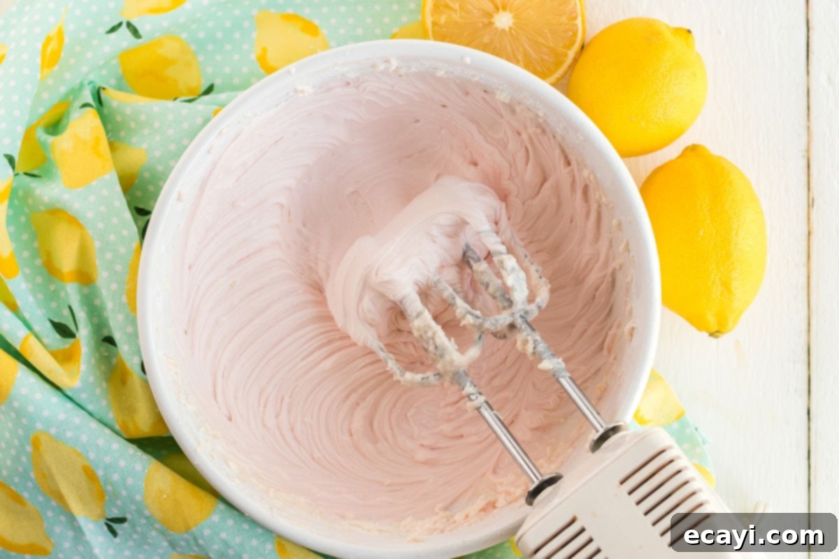 Sparkling Pink Lemonade Cake 12 A mixer blending pink frosting in a bowl, achieving a creamy and smooth consistency for decorating the cake.