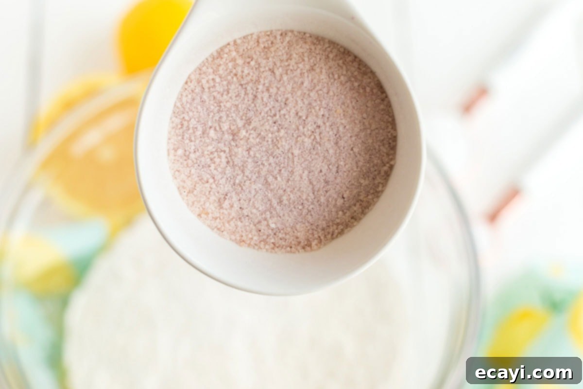 Sparkling Pink Lemonade Cake 4 A hand adding a spoonful of pink lemonade powder to a bowl filled with dry cake ingredients, ensuring even distribution.