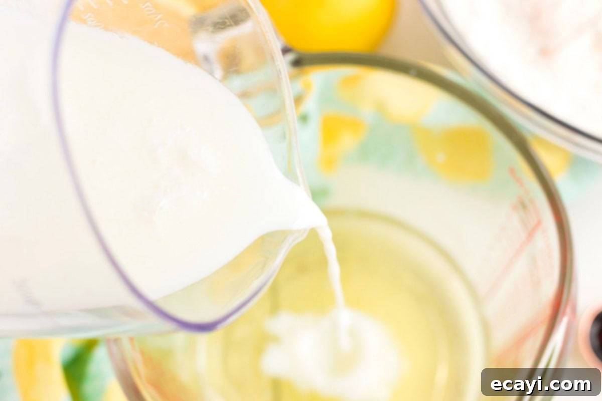 Sparkling Pink Lemonade Cake 5 A hand pouring buttermilk into a mixing bowl, combining it with other wet ingredients for the cake batter.