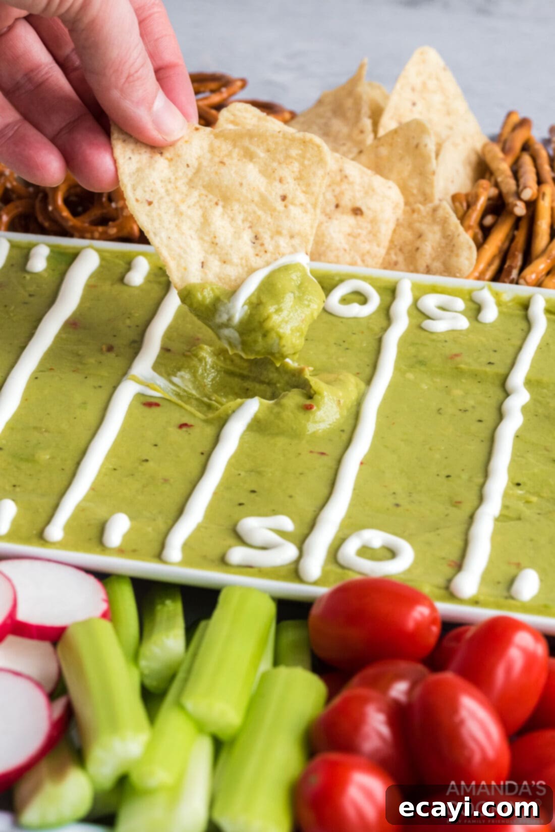 Game Day Grazing Platter 3 Close-up shot of a hand dipping a crispy chip into creamy, fresh guacamole on the football party tray.