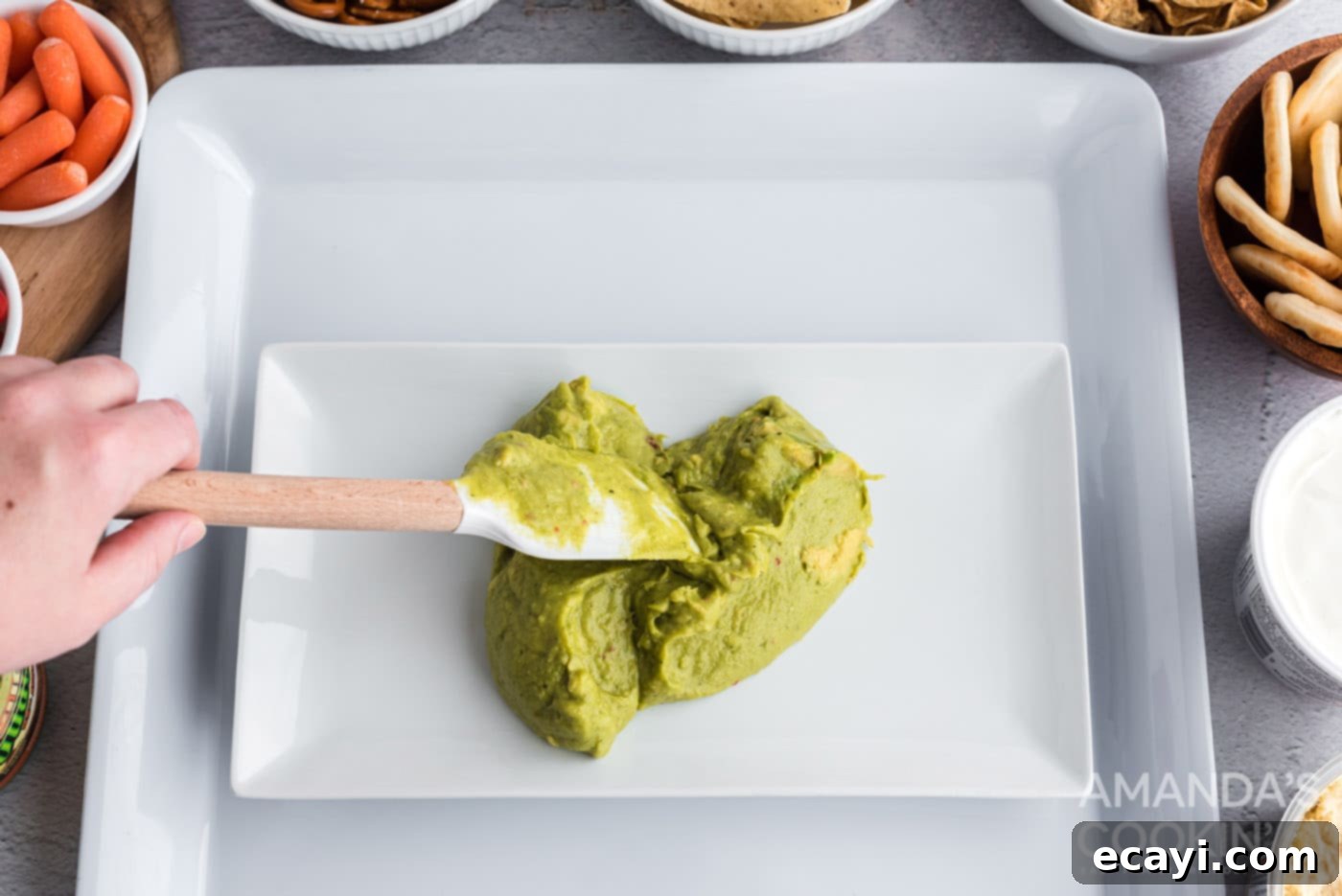 Game Day Grazing Platter 5 Spreading smooth guacamole onto a small round platter to form the base of the football field.