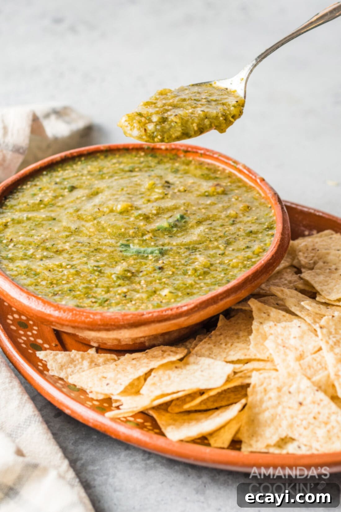 Green Salsa 2 A spoon lifting a scoop of fresh, vibrant green salsa verde from a rustic ceramic bowl, highlighting its perfect texture and rich color.