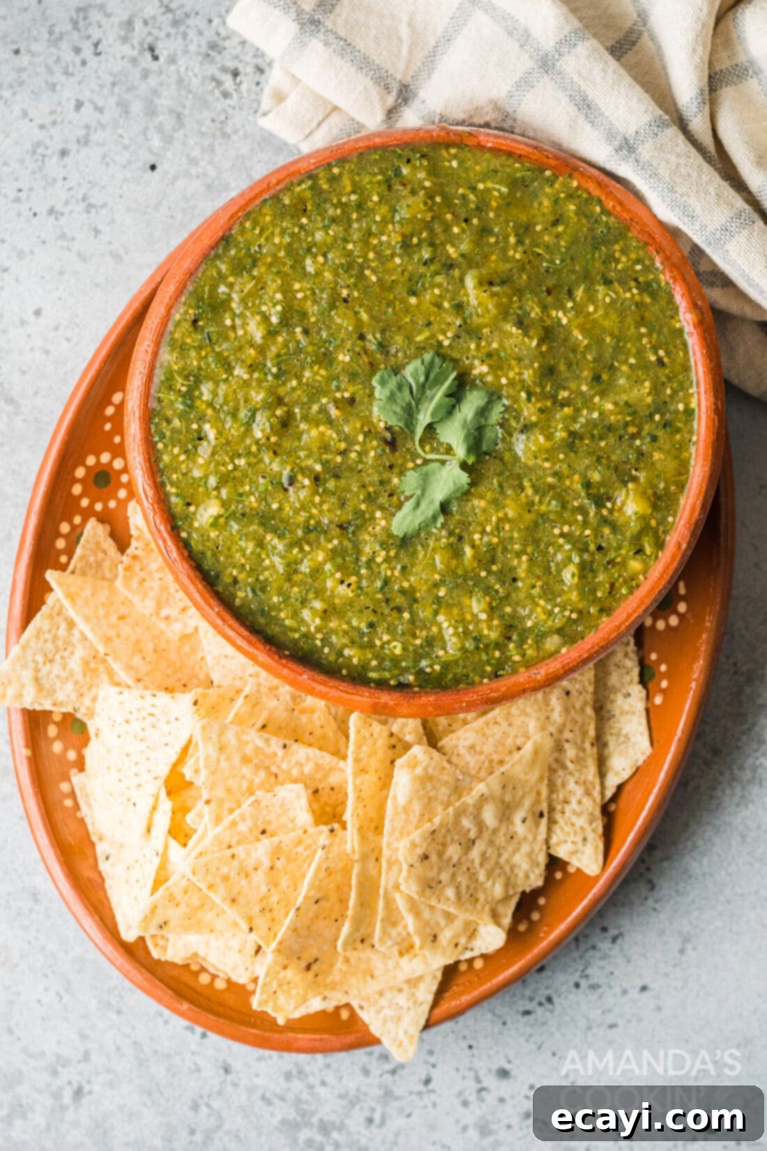 Green Salsa 8 A beautiful ceramic bowl filled with homemade salsa verde, surrounded by a generous pile of crispy tortilla chips, ready for dipping.