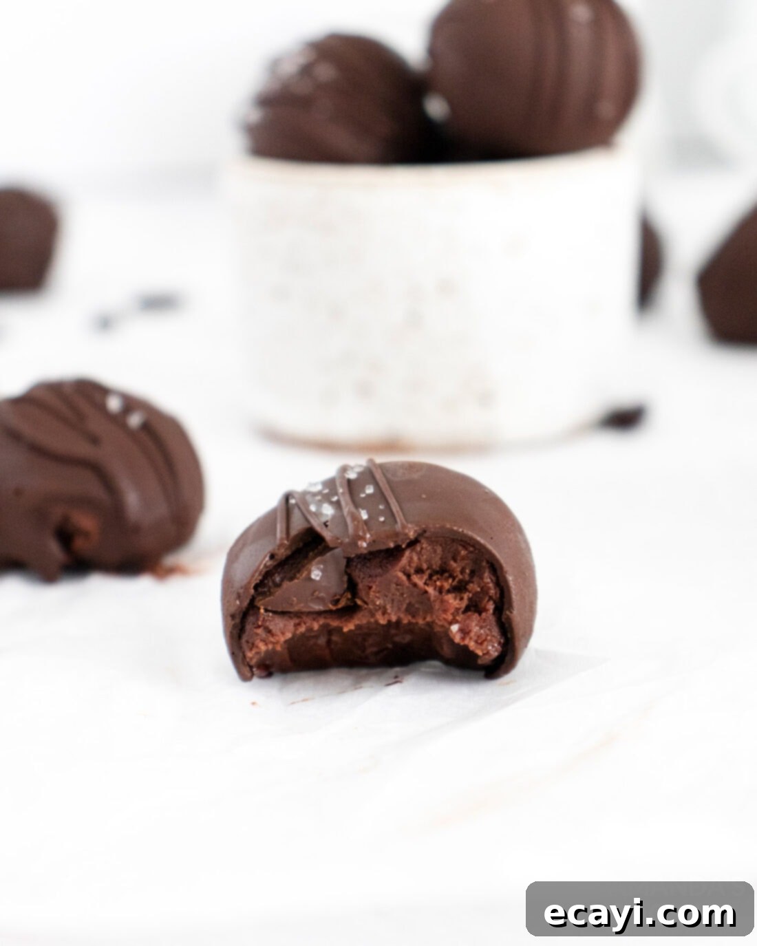 Decadent Mocha Truffles 2 A perfectly formed mocha truffle with a small bite taken out, revealing its rich, dark interior. It sits on a parchment-lined surface, dusted lightly, hinting at its exquisite flavor.