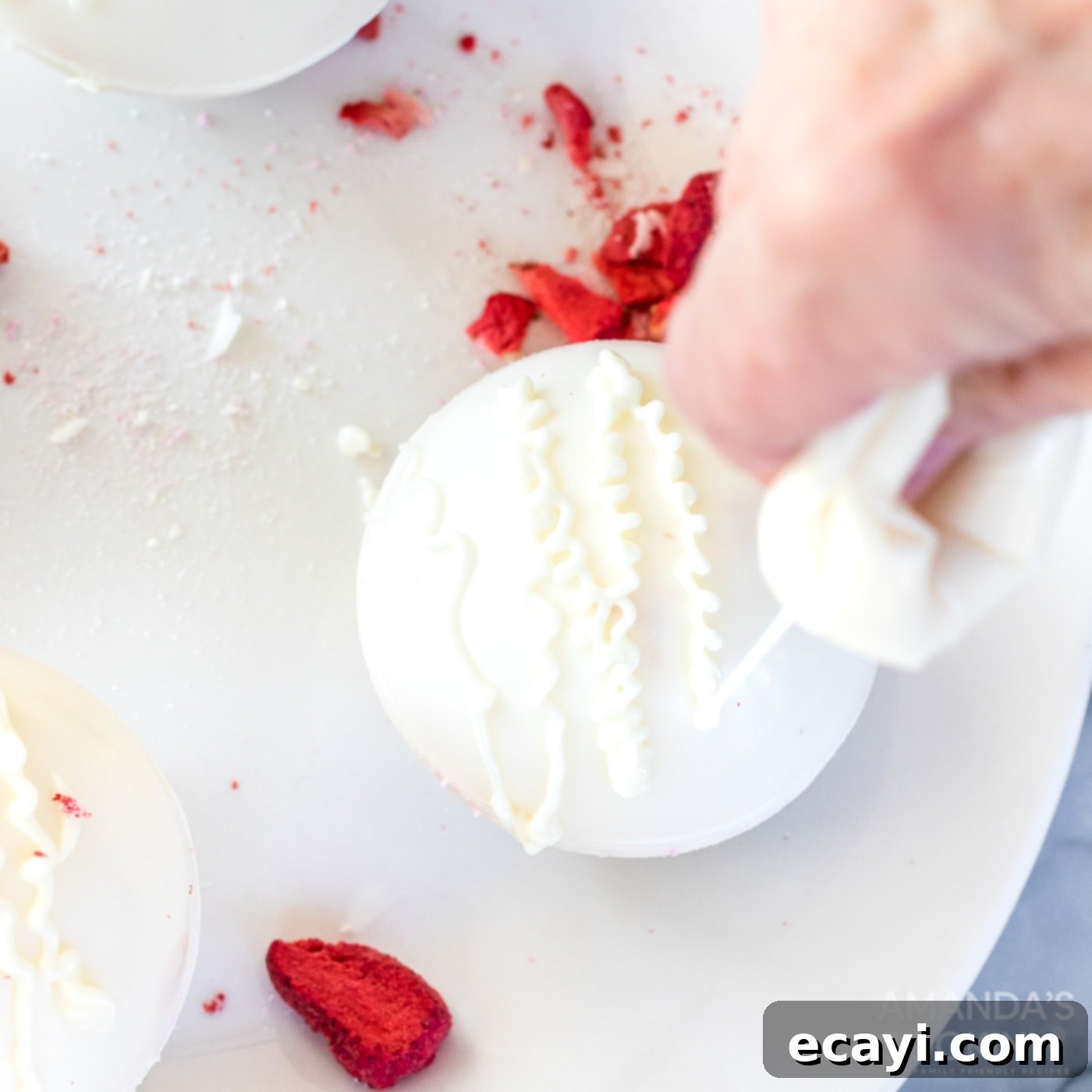 Dreamy Strawberry White Chocolate Hot Cocoa Bombs 13 Decorating the top of a hot cocoa bomb by piping melted white chocolate from a plastic bag, ready for additional sprinkles or dust.