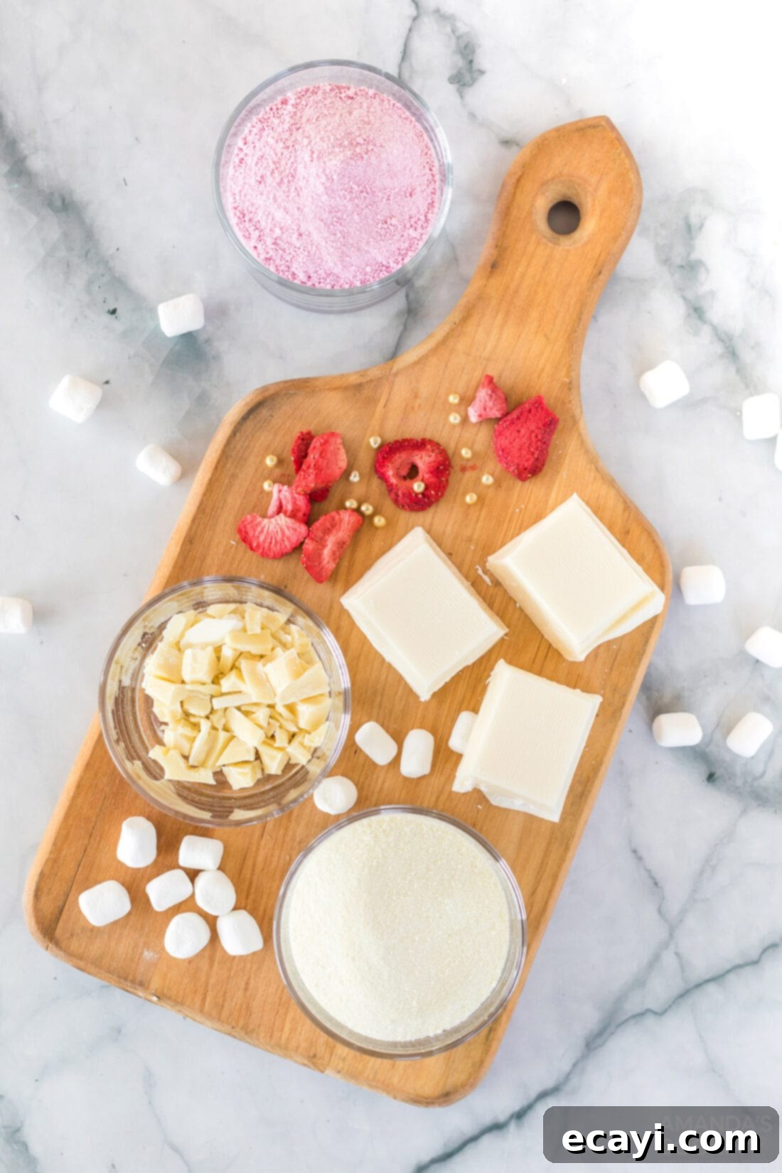 Dreamy Strawberry White Chocolate Hot Cocoa Bombs 4 A vibrant selection of ingredients for white chocolate strawberry hot cocoa bombs, including white chocolate, powdered strawberry drink mix, powdered milk, freeze-dried strawberries, and mini marshmallows, laid out on a clean surface.