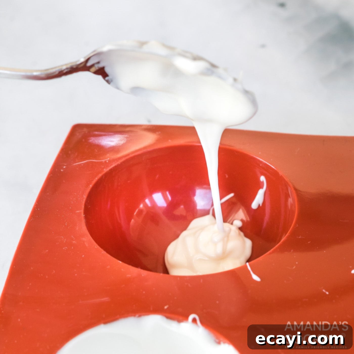 Dreamy Strawberry White Chocolate Hot Cocoa Bombs 7 Spoonfuls of melted white chocolate being carefully spread into silicone sphere molds, forming the outer shells of the hot cocoa bombs.