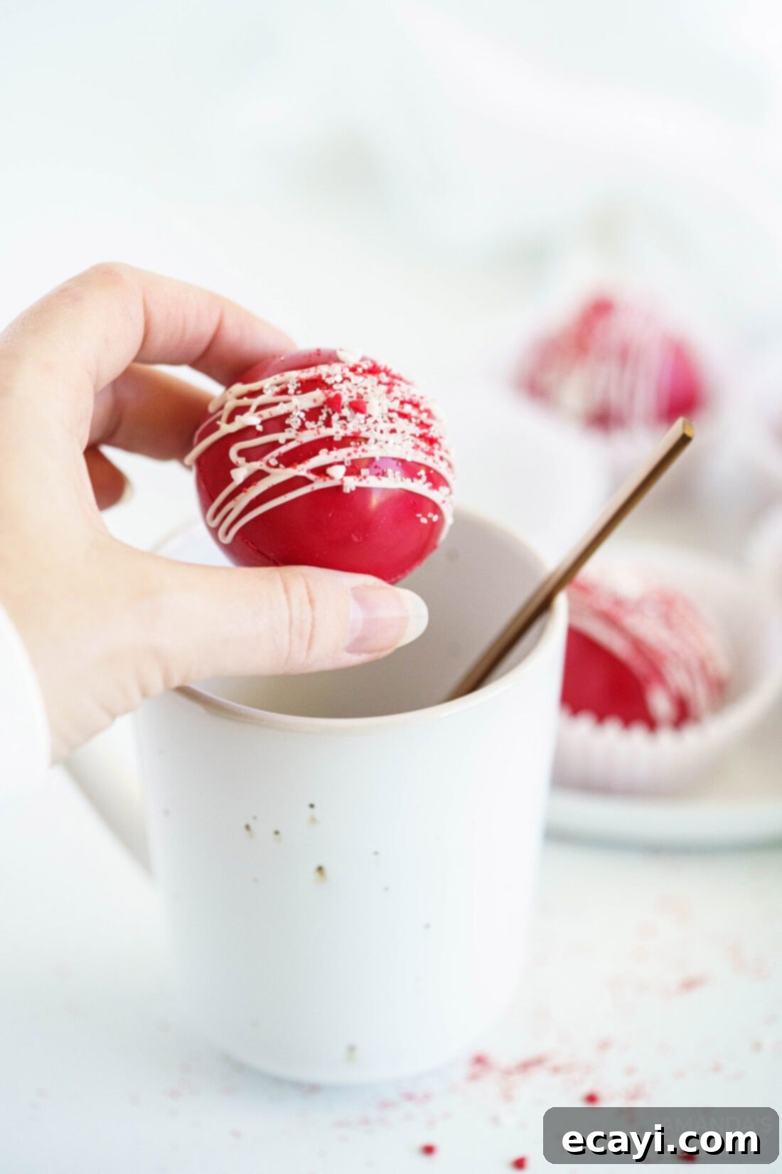 Decadent Red Velvet Hot Cocoa Bombs 2 A woman holding a beautifully crafted red velvet cocoa bomb above a mug, ready to be dropped into hot milk.