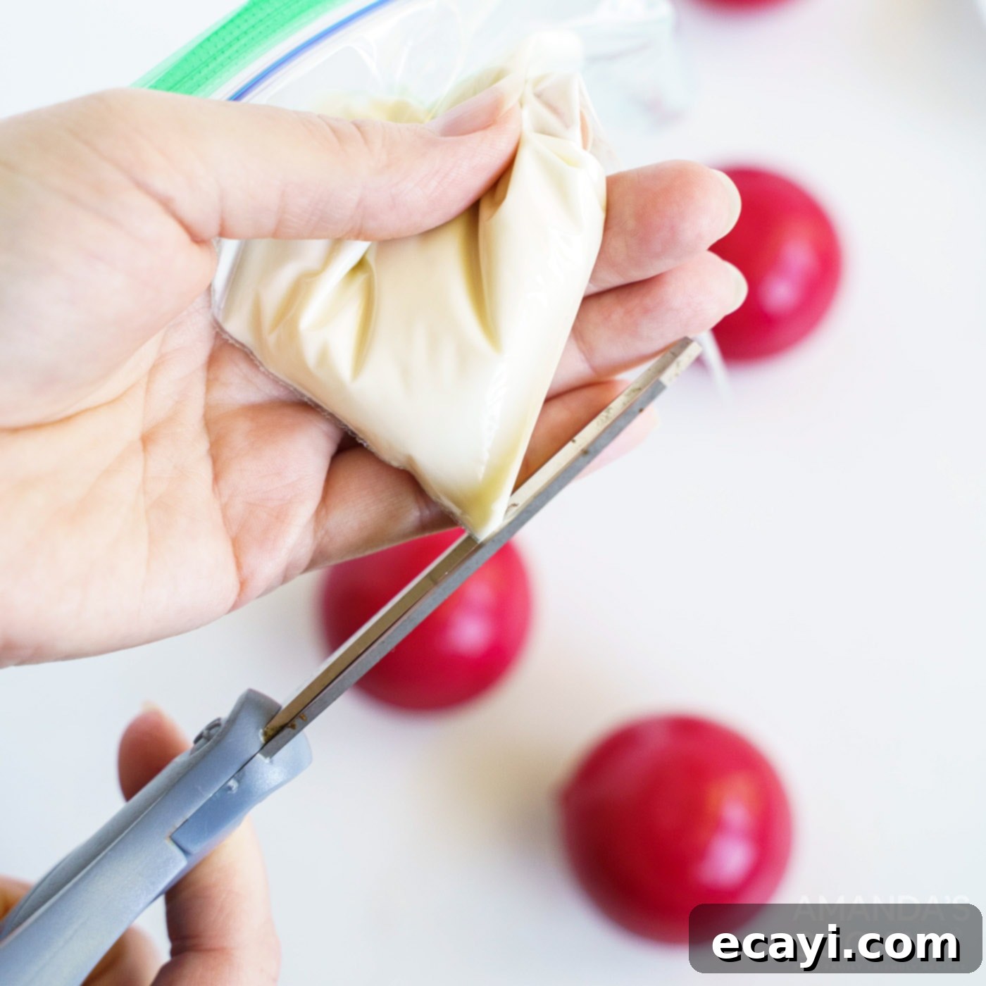 Decadent Red Velvet Hot Cocoa Bombs 11 A hand holding a zip-top plastic bag with melted white candy, demonstrating how to snip a tiny corner for drizzling.