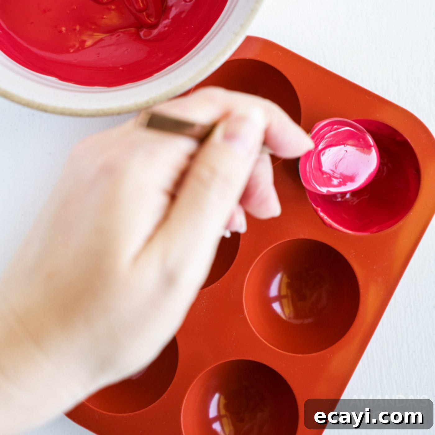 Decadent Red Velvet Hot Cocoa Bombs 6 Melted red candy being carefully spooned into the spherical wells of a silicone mold.