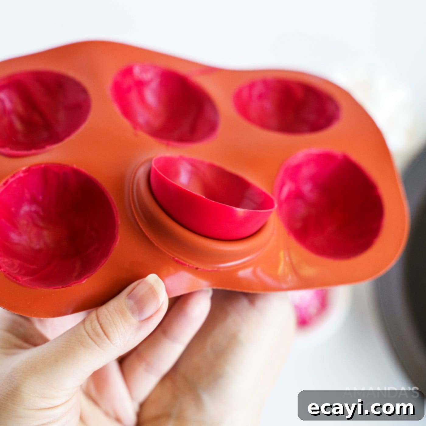 Decadent Red Velvet Hot Cocoa Bombs 7 A hand gently peeling back a silicone mold, revealing a perfectly formed red candy half-sphere for a cocoa bomb.