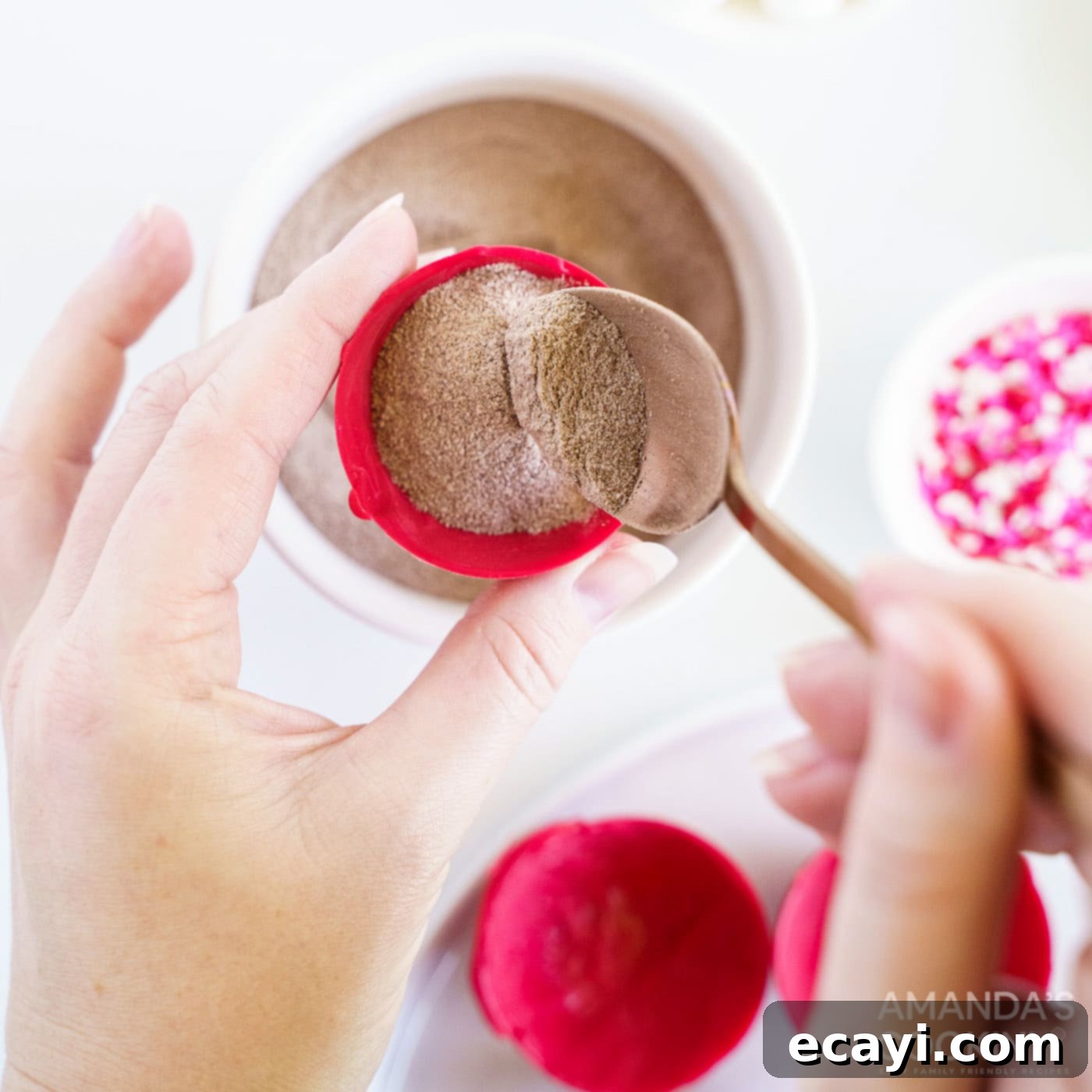 Decadent Red Velvet Hot Cocoa Bombs 8 A close-up of a red candy half-sphere being filled with hot cocoa mix.
