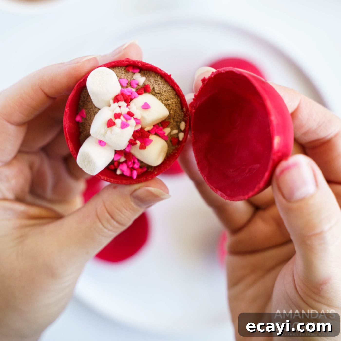 Decadent Red Velvet Hot Cocoa Bombs 10 A hand carefully pressing two red candy half-spheres together on a warm surface to seal them into a complete hot cocoa bomb.