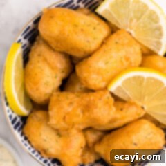 Crispy Golden Beer-Battered Fish 11 A bowl filled with freshly fried, golden beer battered fish nuggets, garnished with a sprig of fresh dill.